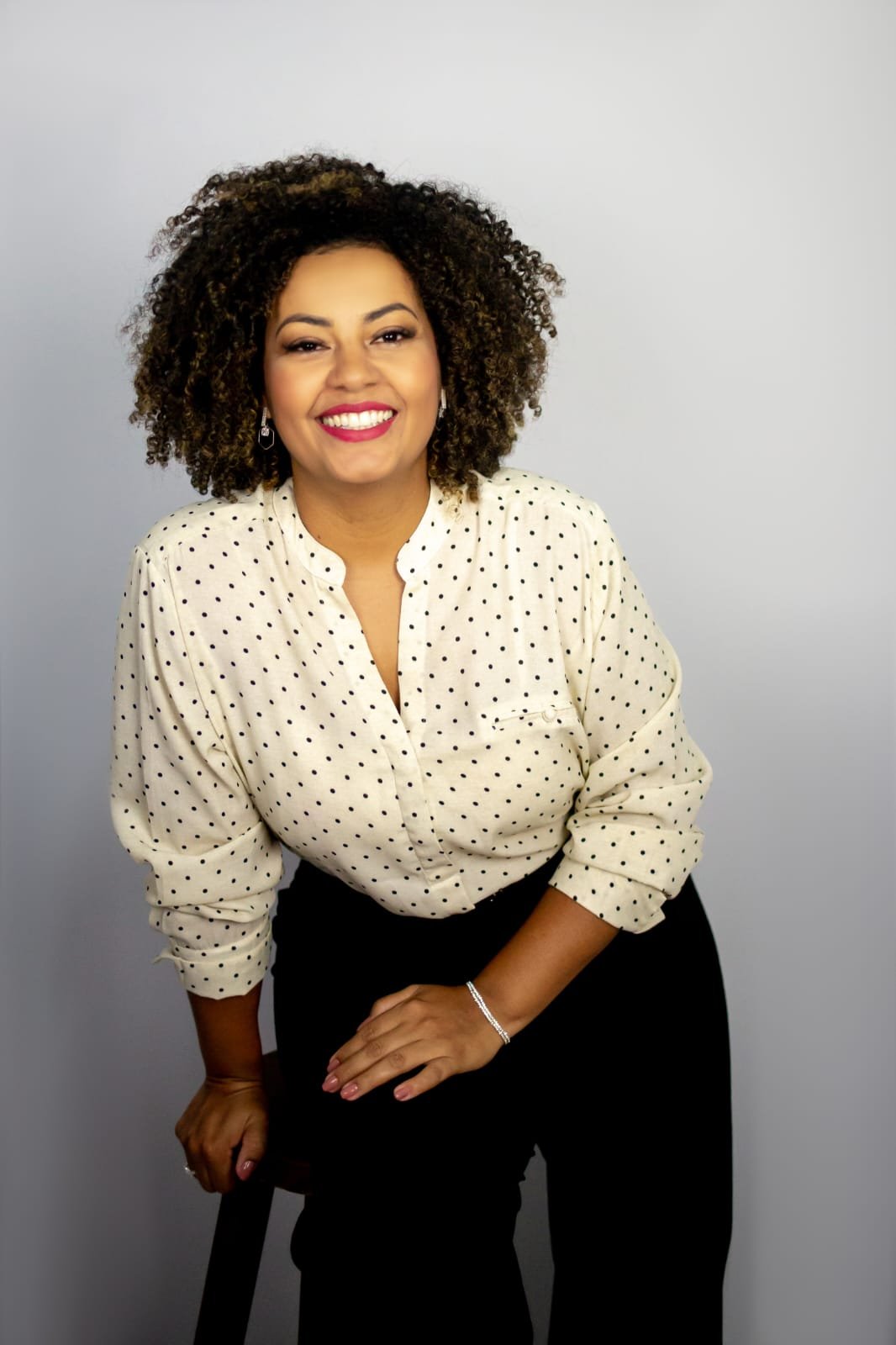 Anna Tavares, linda como sempre, apoiada num banquinho de camisa de poá, dando risada